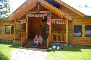 Two people sitting on cabin porch with American flags.