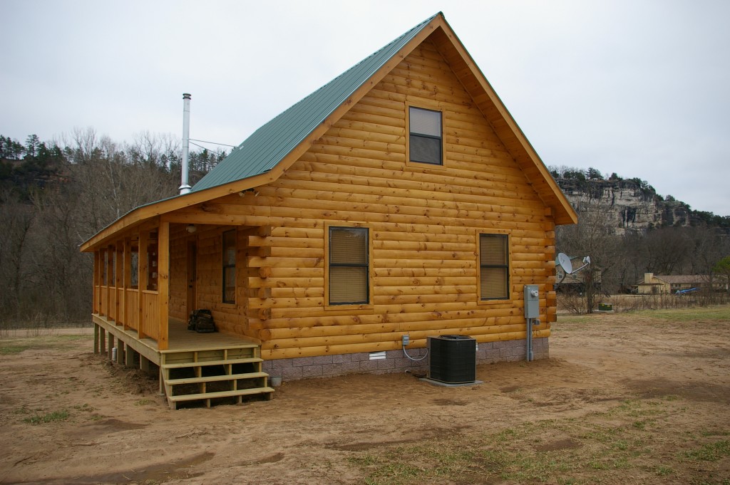 Wooden cabin with porch near rocky cliff countryside.