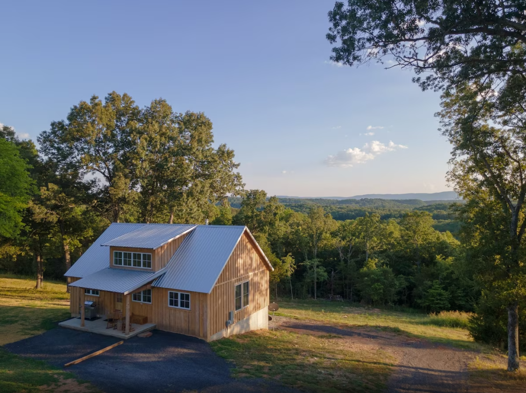 Rustic cabin surrounded by trees with scenic hill view.