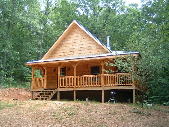 Wooden cabin in forest with front porch.