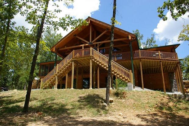 Wooden cabin with wraparound deck in forest.