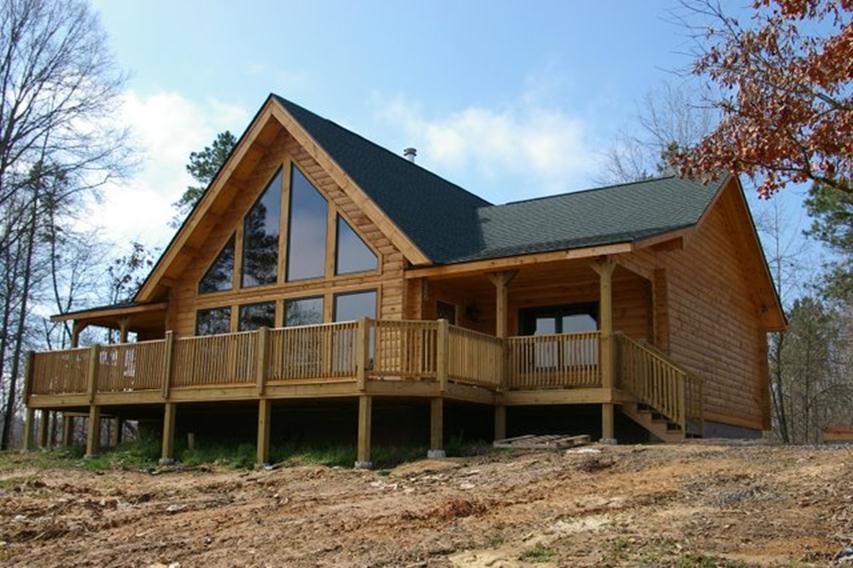 Wooden cabin house with large windows and wraparound deck.
