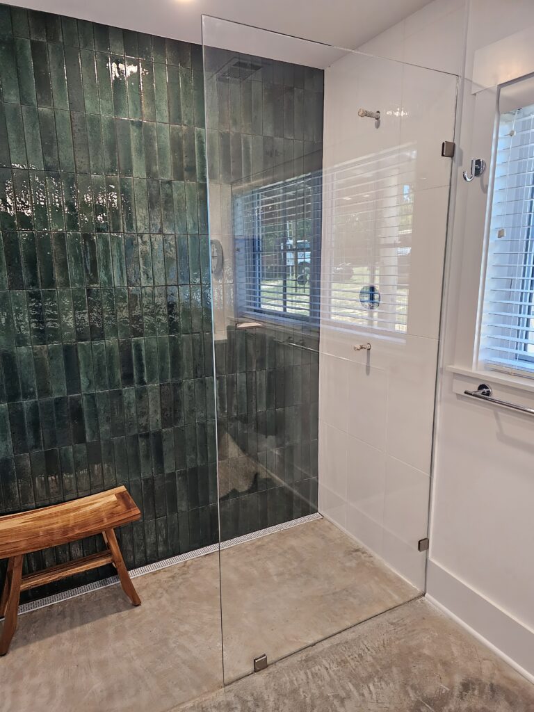 Modern bathroom with glass shower and green tiles.