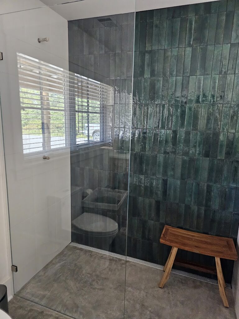 Modern bathroom with glass shower and wooden bench.