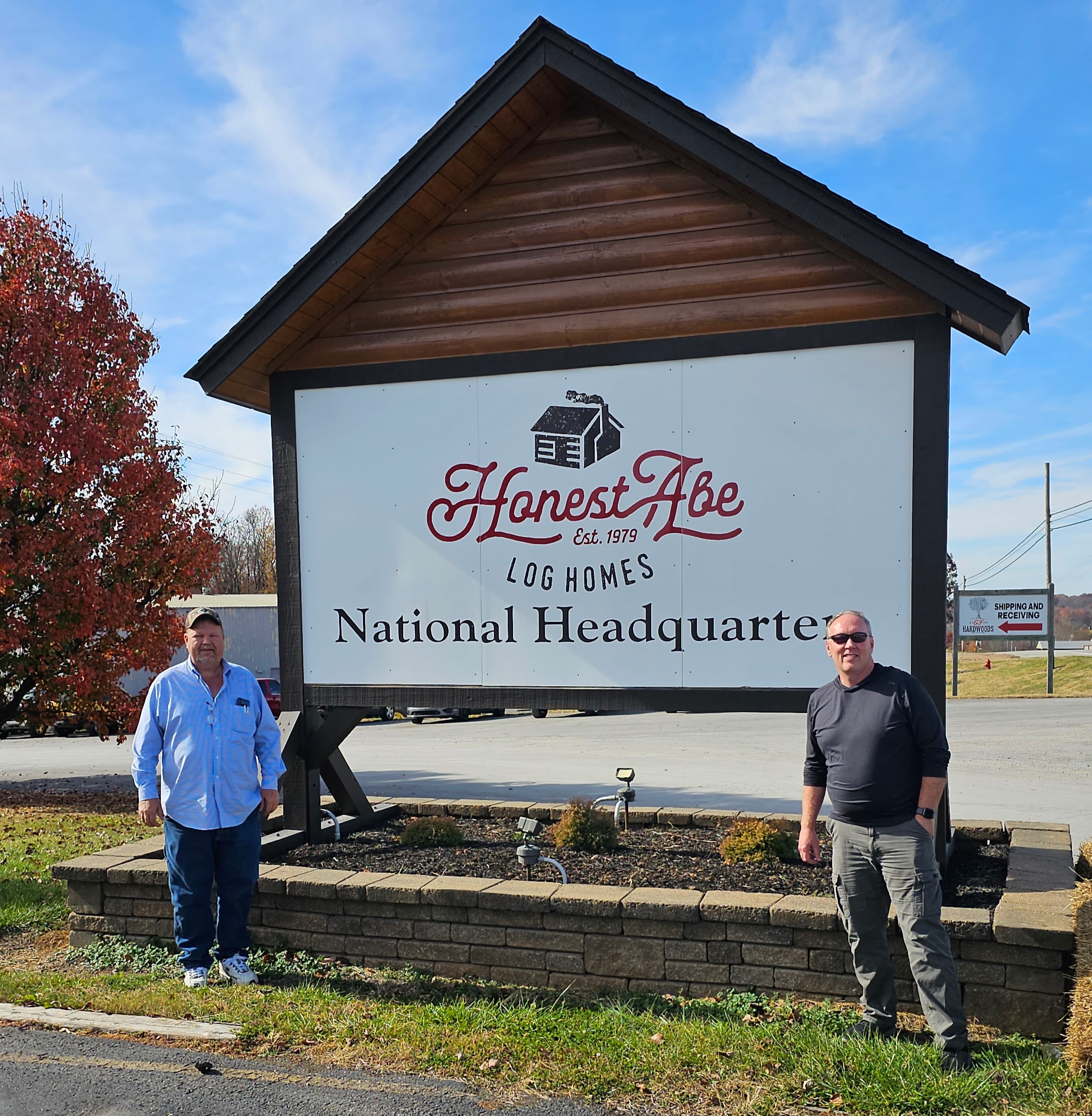 Two men standing by Honest Abe Log Homes sign.